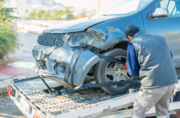 Operario de grúa cargando coche accidentado con daños frontales sobre la plataforma