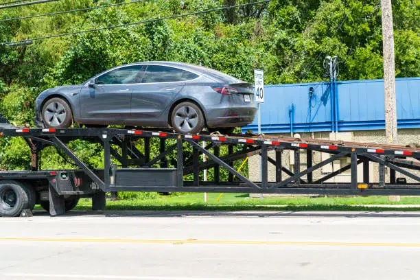 Coche eléctrico Tesla blanco sobre remolque frente a concesionario Tesla